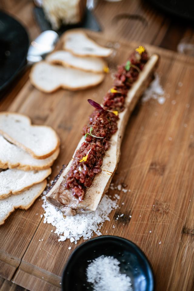 Hueso de tuétano con tartar, tostas de pan y sal en escamas sobre tabla de madera